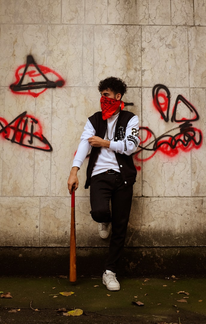 A boy in gang colours learning against a wall with a baseball bat